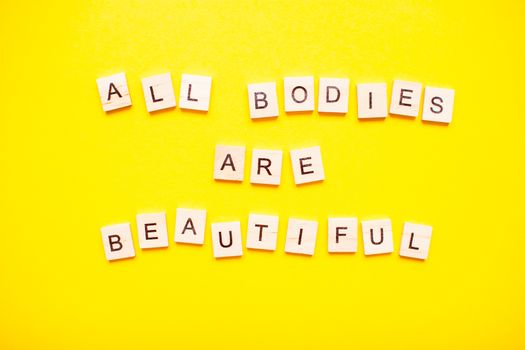 The inscription all bodies are beautiful made of wooden blocks on a light yellow background.