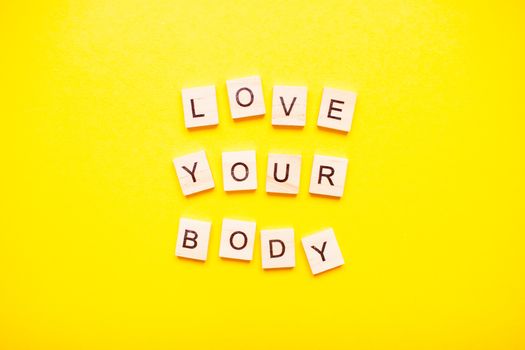 The inscription love your body made of wooden blocks on a light yellow background.