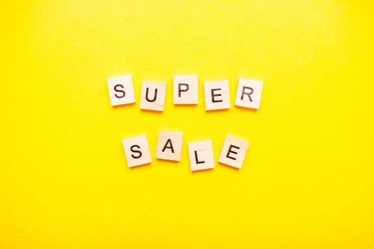 The inscription super sale made of wooden blocks on a light yellow background.