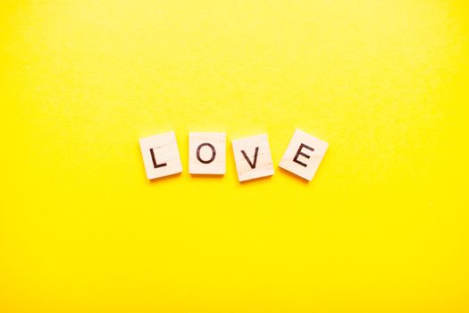 The inscription love made of wooden blocks on a light yellow background.