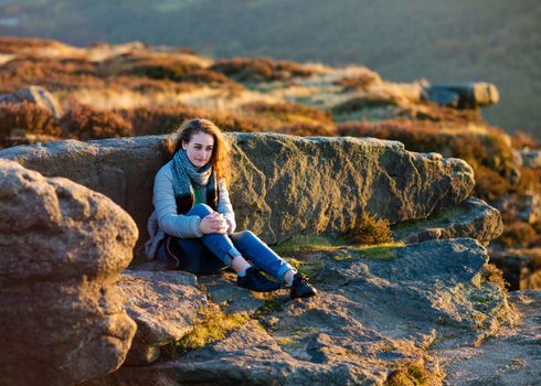 A girl sitting on top of hill against an amazing landscape in the autumn