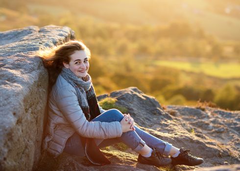 A girl sitting on top of hill against an amazing landscape in the autumn