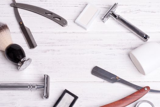 Razors, brush, perfume, balsam and blades on a white wood background.