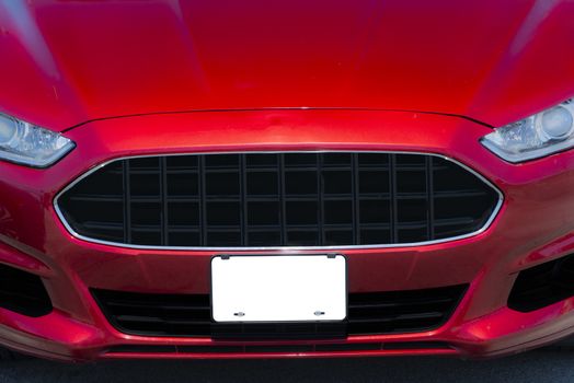 Horizontal shot of a red automobile with a blank white front license plate with copy space.
