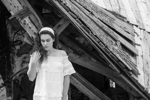 Beautiful young woman in light dress posing standing in front of the ruins of a ghost town