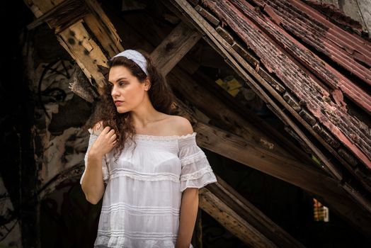 Beautiful young woman in light dress posing standing in front of the ruins of a ghost town