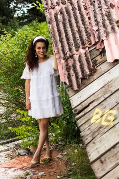 Beautiful young woman in light dress posing standing in front of the ruins of a ghost town