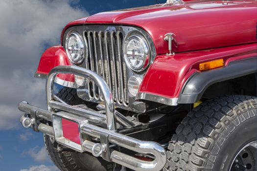 Fragment of a jeep with a front wheel and bumper against a background of white clouds