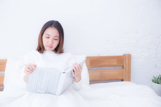 Asian woman reading a book and smiling in bedroom. lifestyle concept.