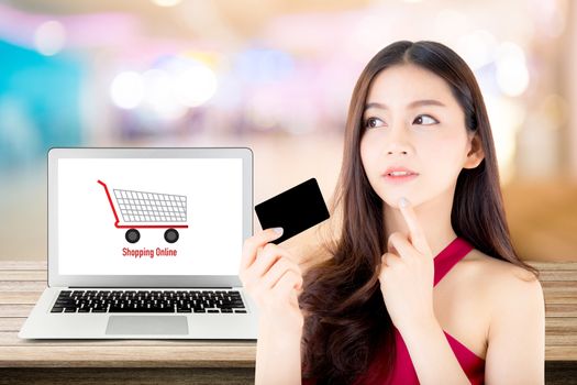 Beautiful woman asia using credit card shopping online with labtop, notebook on table top and bokeh background, girl thinking payment with computer.