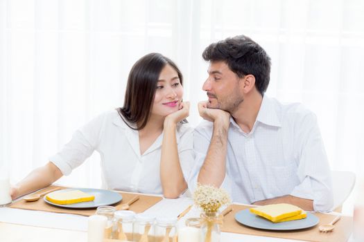 Cheerful asian young man and woman having sitting lunch and talking together at kitchen, family relationship with romantic concept.