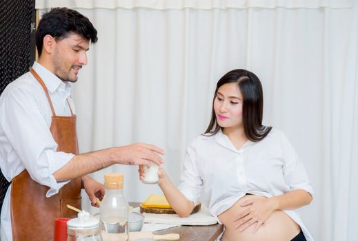 Happy husband and pregnant wife in kitchen,Asian man cooking food in kitchen and woman with drink milk at home,Happy family concept.