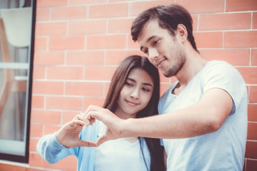 Closeup of young man and woman asian making heart shape with hand, Loving couple with heart shape of hand outdoors.