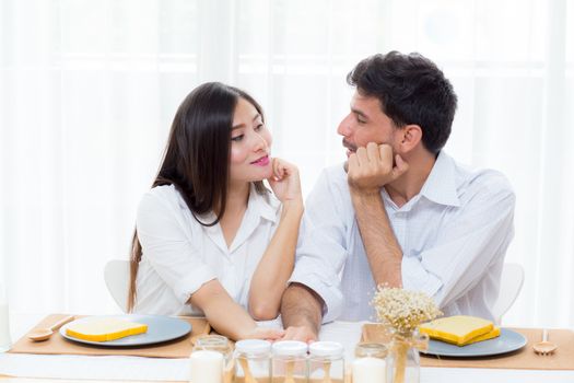 Cheerful asian young man and woman having sitting lunch and talking  together at kitchen