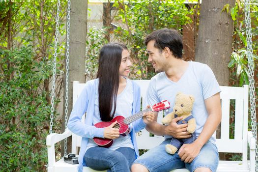 Young asian woman and man couple sitting at park playing ukulele and sing a song outdoors relax concept.