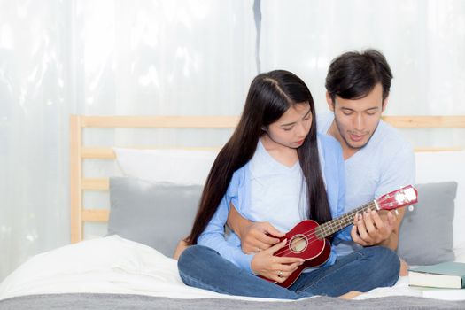 Young Asian couple playing ukulele relaxing with happiness and joyful in bedroom.