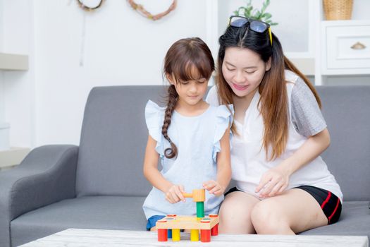 Asian kid girl and mother playing toy block; together with cheerful and happy in living room, activity in family.