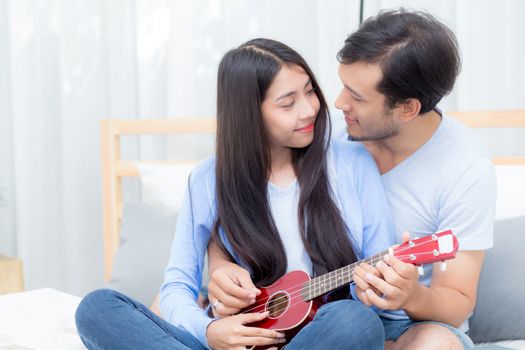 Young Asian couple playing ukulele relaxing with happiness and joyful in bedroom.