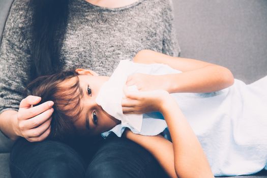 Little asian girl is sick weak lying on sofa with mother of take care and touching forehead in living room - family health concept.