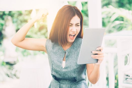 Asian woman looking tablet have a angry and upset outside in the park - expression and stress of communication concept.