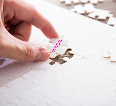 Hand putting the a last piece of white jigsaw puzzle with the word of HOPE. conceptual image