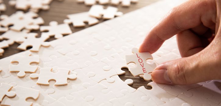 Hand completing the a last piece of jigsaw puzzle with love word. Family love conceptual