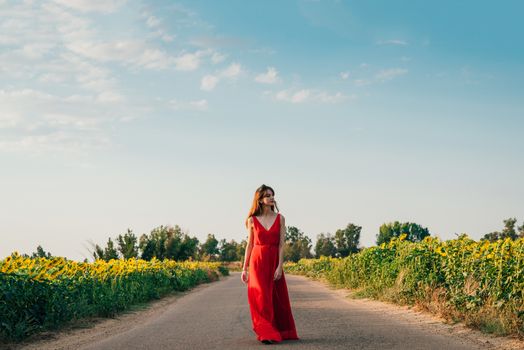 Woman with red dress walking on road with sunflowers.