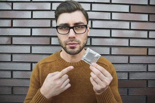 Male youngster with appealing look, holds condom.