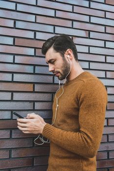 Smiling man listening to music on headphones and leaning against brick wall.