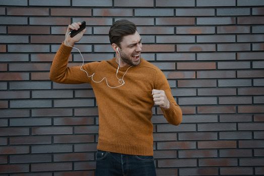 Portrait of smiling man with headphones and cellphone standing by brick wall.