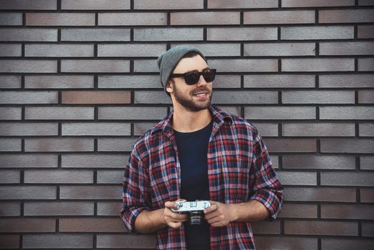 Man with retro photo camera Fashion Travel Lifestyle outdoor while standing against brick wall background.