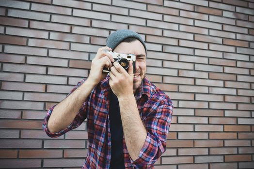 Man with retro photo camera Fashion Travel Lifestyle outdoor while standing against brick wall background.