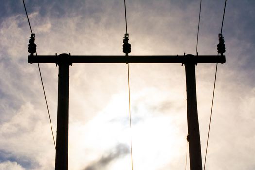 Wooden utility poles in silhouette with electricity wires on a cloudy sky during sunset.