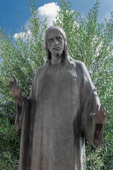 Old bronze Jesus Christ statue in a old cemetery with olive tree in the background
