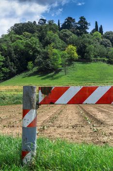 A red and white barrier blocks access to a cultivated field.