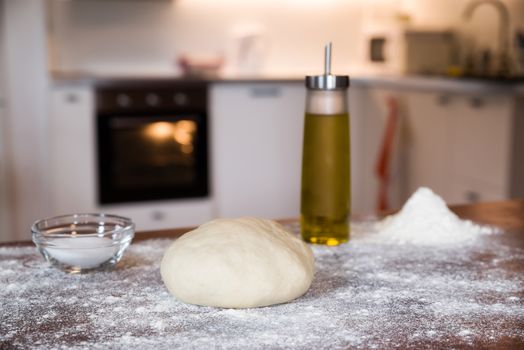 Dough for pizza over a wooden table in a home kitchen