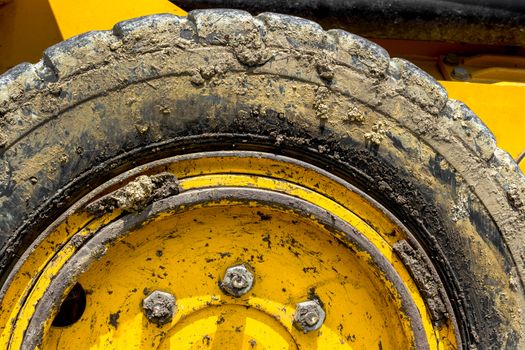 Extreme close up of tire bulldozer, yellow and covered with mud.