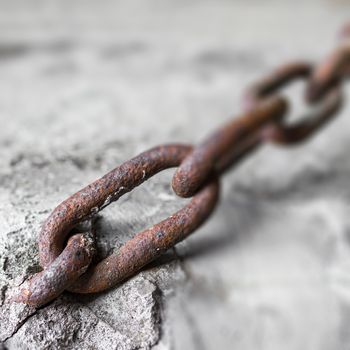 Rusty chain anchored to the cement pole. Defocused blurry background.