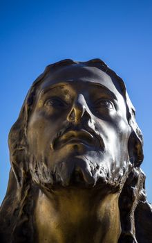 Bronze statue of christ in a blue sky background. Jesus looks up to heaven. Space for the text.