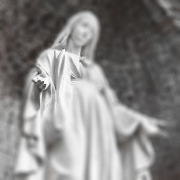 Blurred image of Virgin Mary statue. Selected focus on her hand and heart.