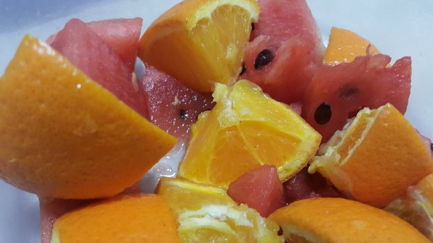 Closeup view of mixed fruits slices of oranges and red water melon served in a ceramic white plate. Water melon is sweet while oranges are citrus in taste