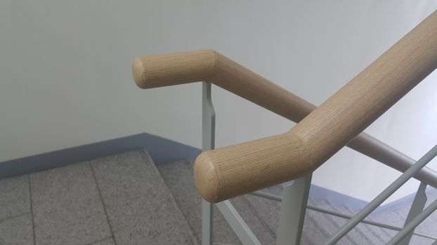 Closeup view of wooden handrail of grey concrete stairs in a modern building. Handrails help people avoiding accidents while moving on stairs.