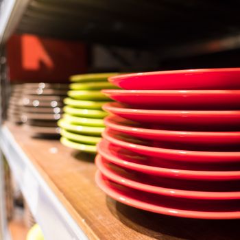 Colored dishes (red, green and white) on a wooden bookshelf, on a blurred background.