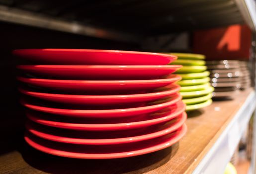 Colored dishes (red, green and white) on a wooden bookshelf, on a blurred background.