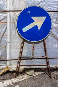 Old mandatory direction sign with scratches and dents in construction site.