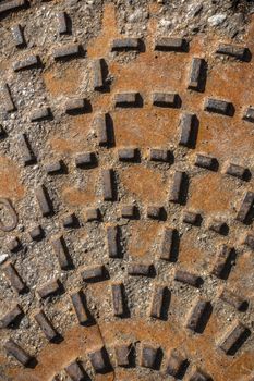 Relief pattern of rusty manhole cover in closeup.
