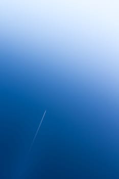 Airplane flying at high altitude leaving its white wake over blue sky