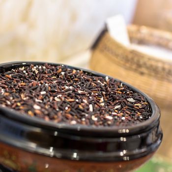 Uncooked black rice in ceramic bowl. Defocused blurry background.