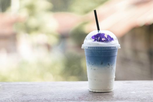 Closeup glass of ice butterfly pea latte on wood table with nature background