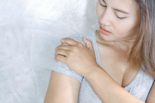 Closeup woman hand holding shoulder with pain on grey background